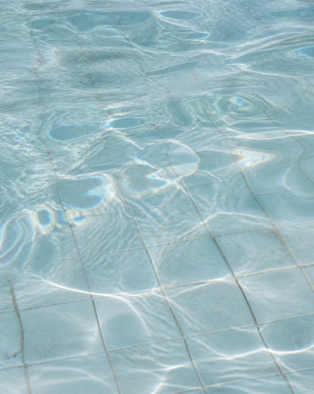 Sunlight refracting across clear pool water and pale tiles